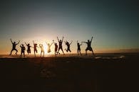 Silhouette of a group of friends jumping on a beach at sunset, expressing joy and freedom.